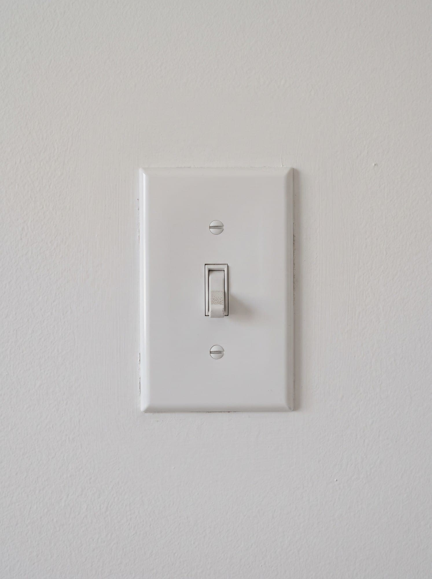 A plain white plastic light switch plate on a flat white wall