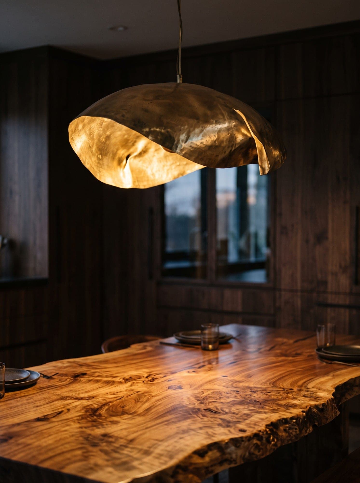 A hand-hammered brass pendant glowing above a live-edge burl wood table