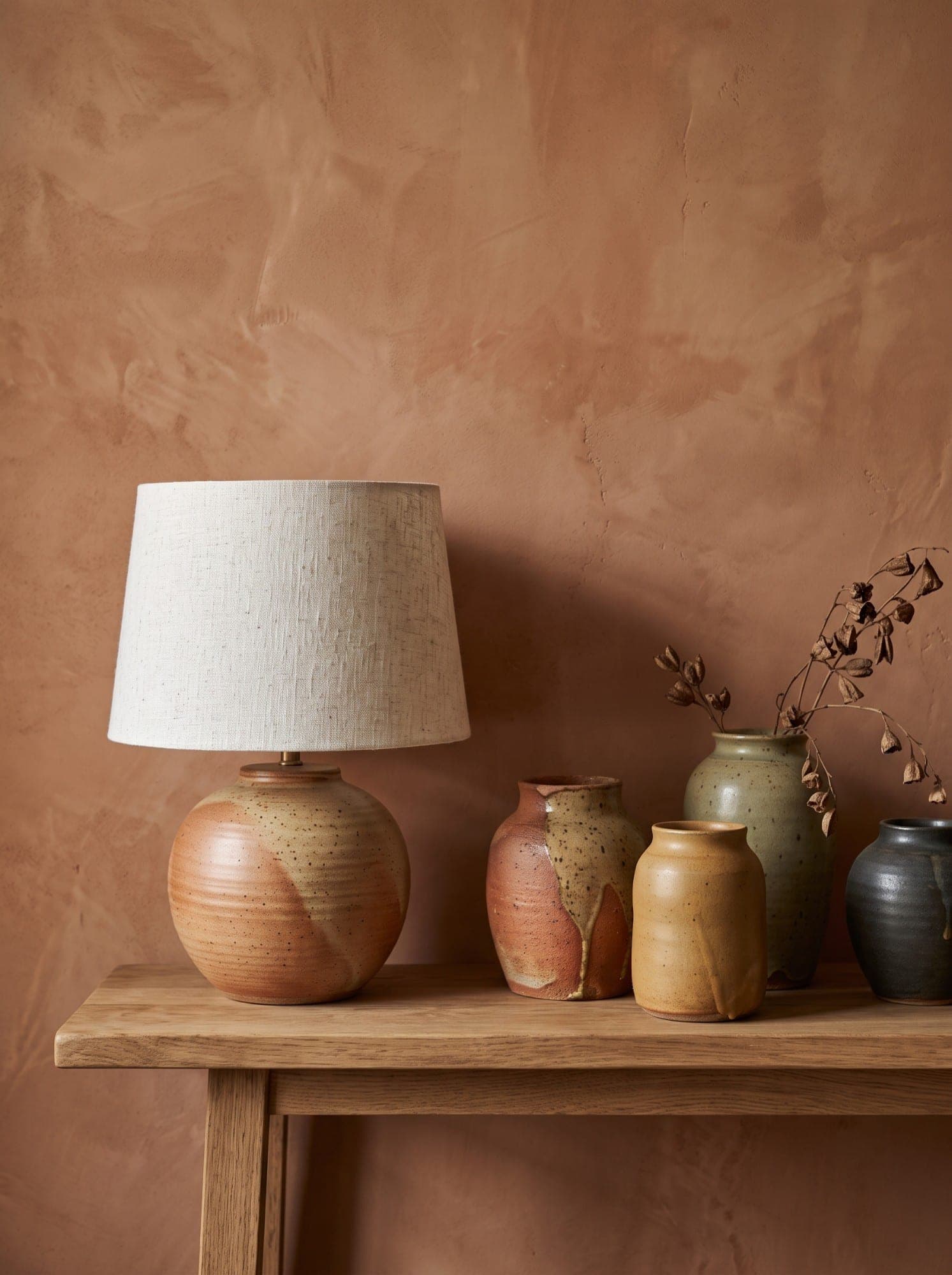 A pottery lamp and hand-thrown vessels on an oak console against a terracotta plaster wall