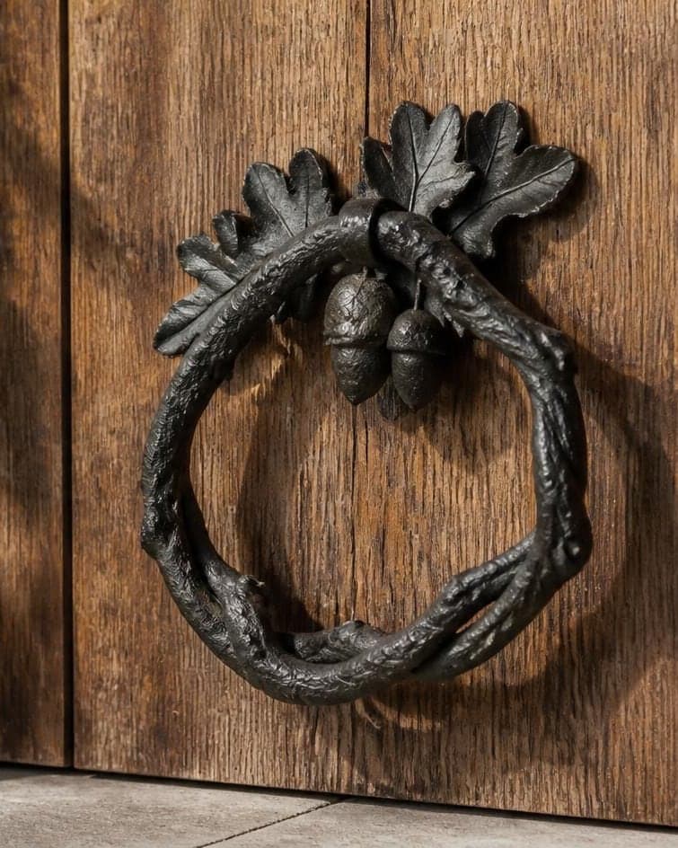 A cast-iron door knocker of oak leaves and acorns wrapped into a ring, on a weathered oak door